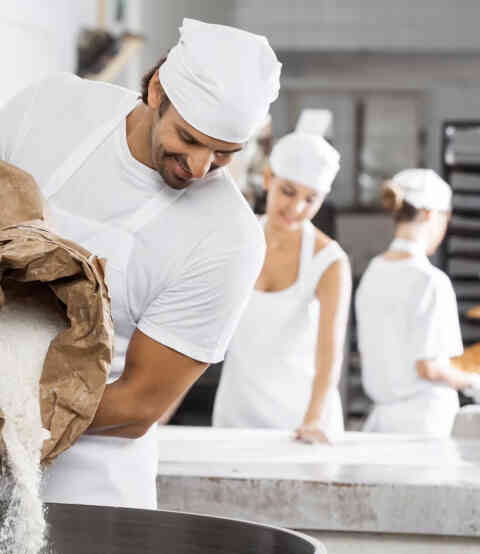 Baker pouring flour in kitchen